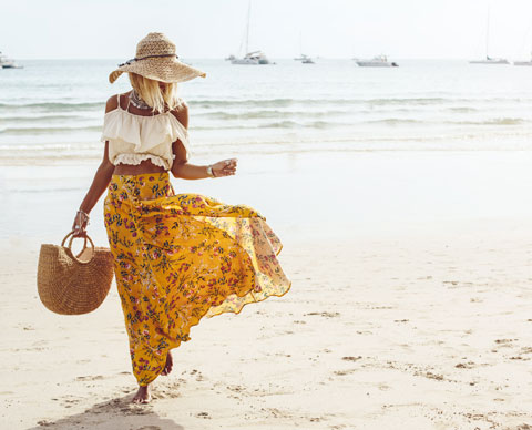 Kvinne på strand med hvit topp og gult skjørt